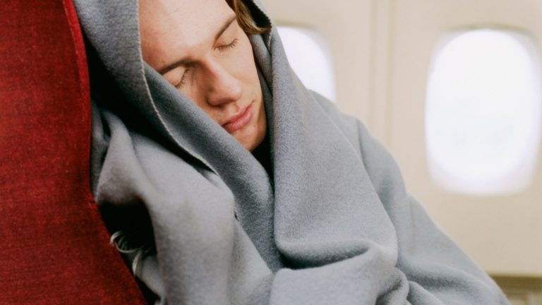 пассажир под пледом в самолете спит у иллюминатора